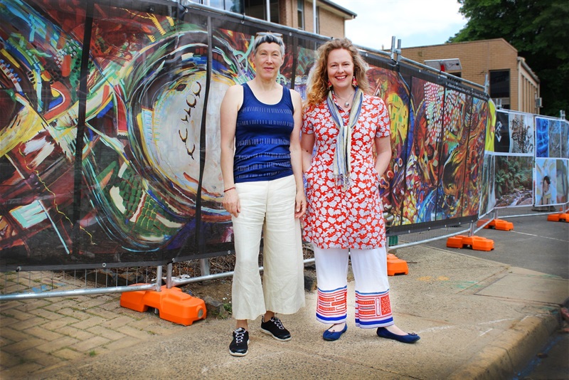Artists Sue Acheson and Bec Van Dyk stand in front of pop up display, wide shot